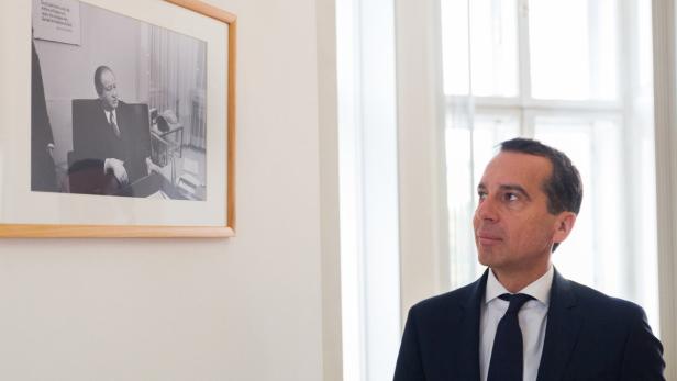 Ein Mann im Anzug blickt auf ein gerahmtes Schwarzweißfoto an der Wand.