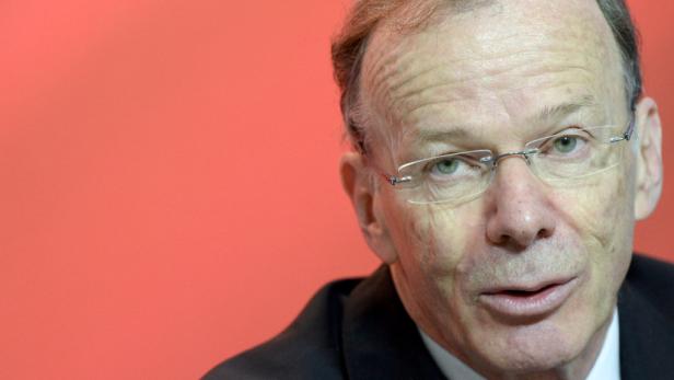 Ein Mann mit Brille vor einem roten Hintergrund.