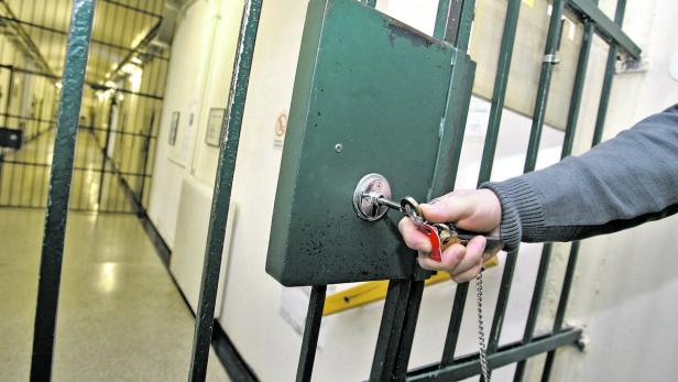 Eine Hand schließt ein Gefängnisgitter mit einem Schlüssel auf.