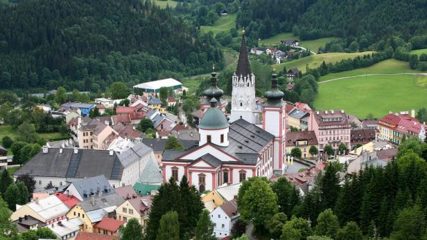 Blick auf eine Stadt mit einer markanten Kirche und bewaldeten Hügeln im Hintergrund.