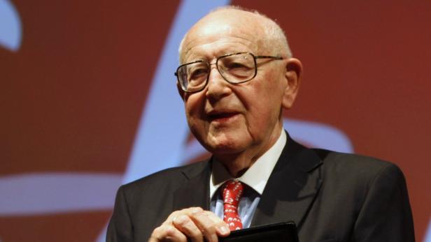 Ein älterer Mann mit Brille und Anzug lächelt.