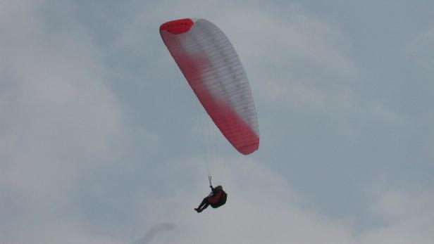 Ein Gleitschirmflieger mit einem rot-weißen Schirm am Himmel.