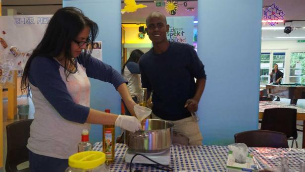 Eine Frau gießt Öl in einen Topf, während ein Mann danebensteht und lächelt.