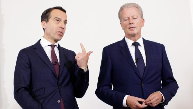 Zwei Männer in Anzügen stehen vor einem weißen Hintergrund.