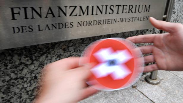 Vor dem Finanzministerium NRW dreht eine Hand einen Kreisel mit Schweizerkreuz.