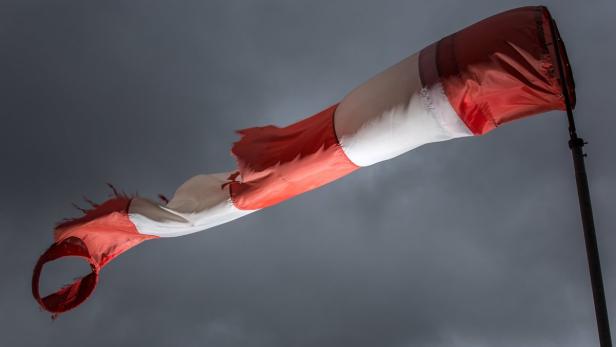 Ein rot-weißer Windsack weht vor einem dunklen, bewölkten Himmel.