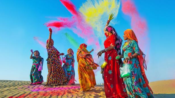 Frauen in traditioneller Kleidung feiern Holi mit Farbpulver in der Luft.