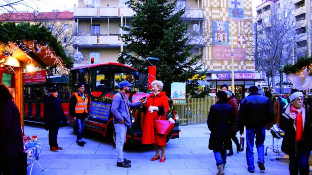 Eine Frau in rotem Mantel wird auf einem Weihnachtsmarkt interviewt.