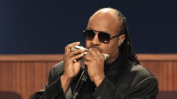 Stevie Wonder spielt Mundharmonika und singt in ein Mikrofon.