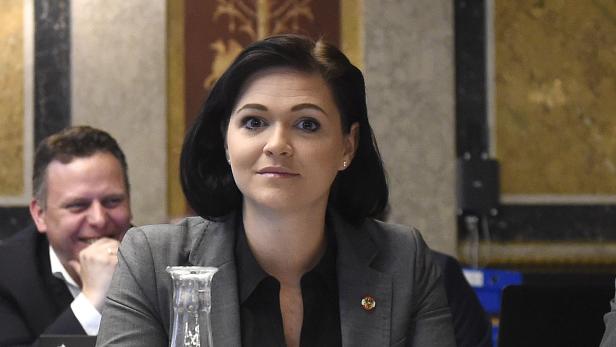 Eine Frau mit dunklen Haaren in einem grauen Blazer sitzt an einem Tisch.