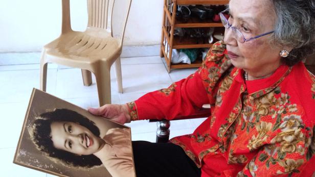 Eine ältere Frau betrachtet ein altes Foto einer jungen Frau.