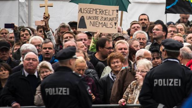 Eine Menschenmenge demonstriert mit Schildern, darunter eines mit der Aufschrift „Ausgemerkelt! Unsere Zukunft? Niemals!“.