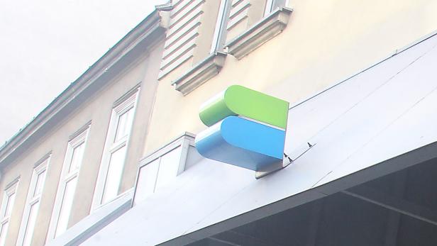 Ein grünes und blaues Logo hängt an der Fassade eines Gebäudes.