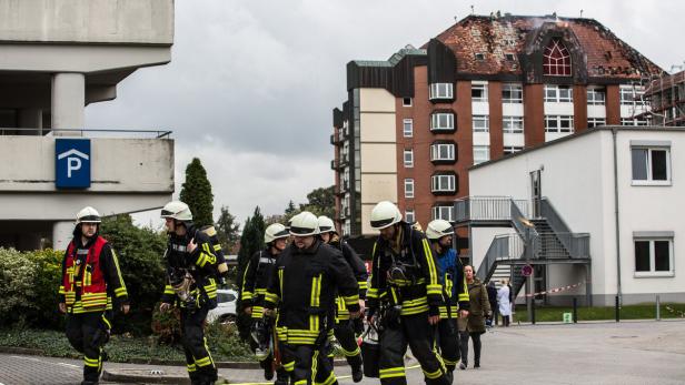 Eine Gruppe Feuerwehrleute geht vor einem beschädigten Gebäude entlang.