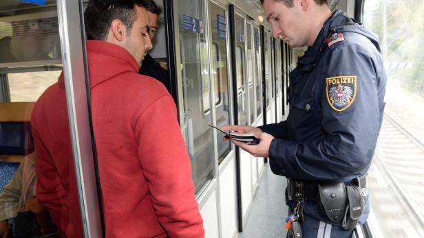 Ein österreichischer Polizist kontrolliert die Ausweise von Fahrgästen in einem Zug.
