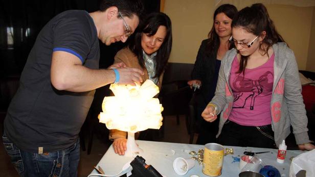 Eine Gruppe von Personen bastelt gemeinsam an einer Lampe aus recycelten Materialien.