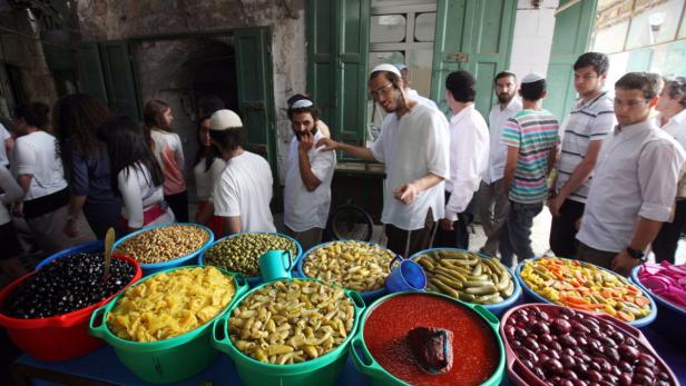 epa03225666 A group of Jewish settlers, protected by Israeli soldiers (unseen), go by a pickles shop in the Old Quarter of the West Bank city of Hebron, 19 May 2012, to allow them to move securely in the area. A few hundred hard-line Jewish settlers live under heavy Israeli military protection in the heart of the city of 170,000 mostly Muslim Palestinians. EPA/ABED AL HASHLAMOUN