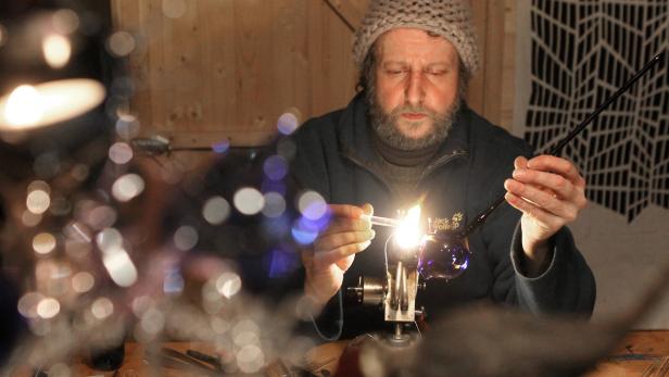 Ein Mann mit Bart formt Glas mit einer kleinen Flamme.
