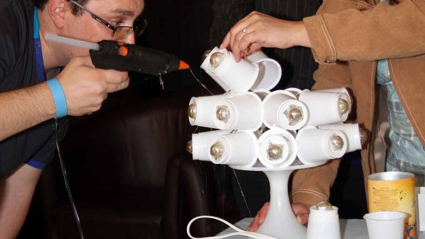 Drei Personen basteln eine Lampe aus Plastikbechern und einer Heißklebepistole.