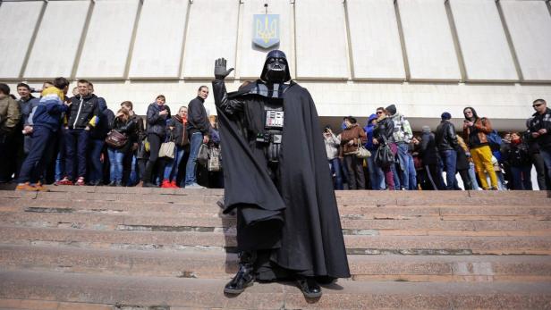 Eine Person in einem Darth Vader Kostüm steht vor einem Gebäude mit einer Menschenmenge.