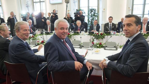 Mehrere Männer in Anzügen sitzen an einem Tisch während einer Konferenz.