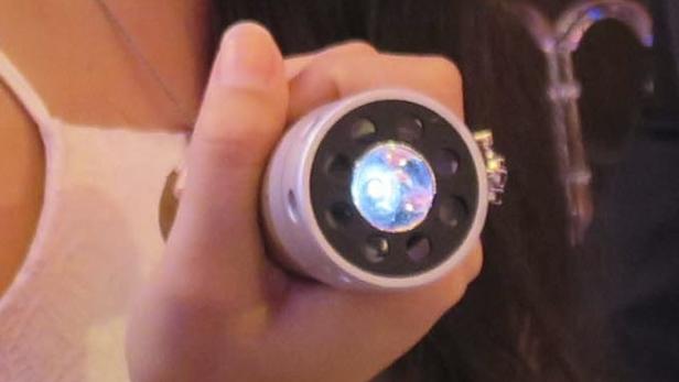 Eine Hand hält eine kleine, runde Taschenlampe mit blauem Licht.