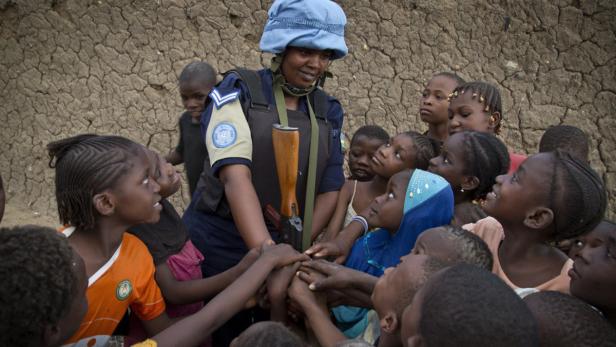 Eine UN-Polizistin umringt von einer Gruppe afrikanischer Kinder, die ihre Hände zusammenlegen.