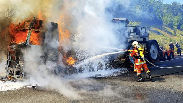 Ein Feuerwehrmann löscht einen brennenden LKW auf einer Autobahn.
