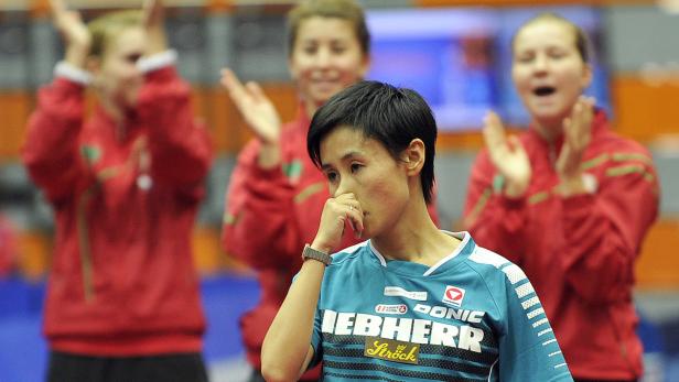 Eine Tischtennisspielerin wirkt nachdenklich, während ihre Teamkollegen im Hintergrund applaudieren.