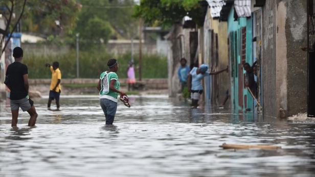 Menschen waten durch eine überflutete Straße in einem Wohngebiet.