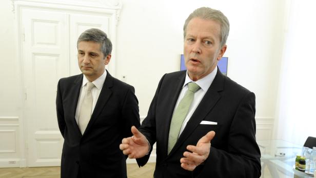 Zwei Männer in Anzügen stehen in einem hellen Raum.