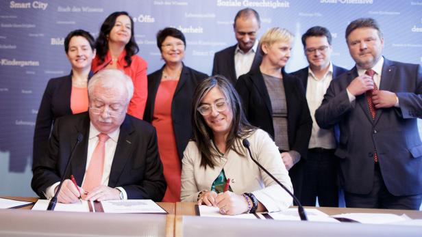 Mehrere Personen unterzeichnen ein Dokument vor einer Wand mit dem Aufdruck „Smart City“.