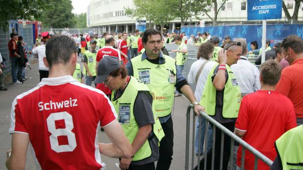 Eine Menschenmenge, darunter Fans im Schweizer Trikot und Ordner mit gelben Westen, vor einem Gebäude.