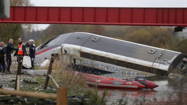 Ein verunglückter Test-TGV liegt unter einer roten Brücke im Wasser, umgeben von Einsatzkräften.