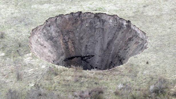 Ein großes Erdloch in einer grasbewachsenen Landschaft.