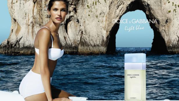 Eine Frau in weißer Bademode posiert vor einem Felsenbogen für eine „Dolce & Gabbana Light Blue“-Werbung.