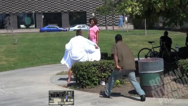 Eine Person in einem weißen Gewand steht in einem Park, während andere Personen zusehen.