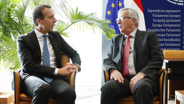 Zwei Männer in Anzügen unterhalten sich vor einer EU-Flagge.