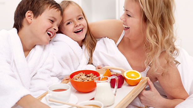 Eine Mutter und ihre Kinder lachen mit einem Frühstückstablett im Bett.