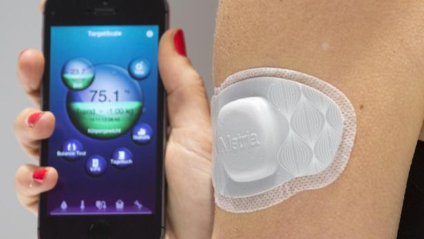 Eine Frau hält ein Smartphone mit einer Gesundheits-App und trägt einen Metria-Sensor am Arm.