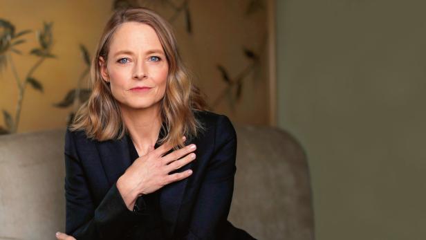 Jodie Foster in einem dunklen Blazer posiert vor einem gemusterten Hintergrund.