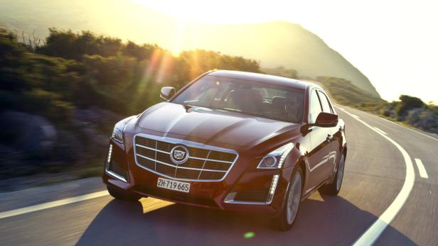 Ein roter Cadillac fährt auf einer kurvenreichen Straße in Richtung Sonnenuntergang.