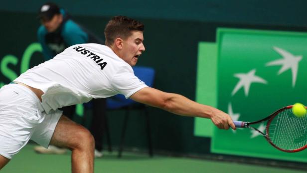 Ein Tennisspieler mit dem Aufdruck „Austria“ auf dem Rücken schlägt einen Ball.
