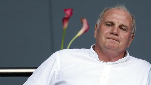Uli Hoeneß in einem weißen Hemd vor einem grauen Hintergrund mit Blumen.