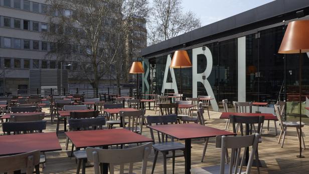 Ein Außenbereich eines Cafés mit Tischen und Stühlen auf einer Holzterrasse.