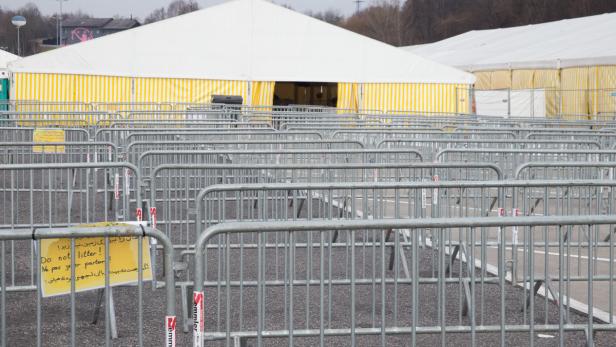 Ein Labyrinth aus Absperrgittern führt zu einem Zelt mit gelb-weissen Streifen.