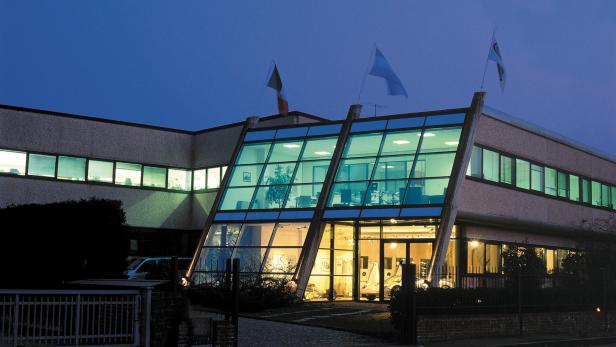 Ein modernes Bürogebäude mit Glasfassade und italienischer Flagge bei Dämmerung.