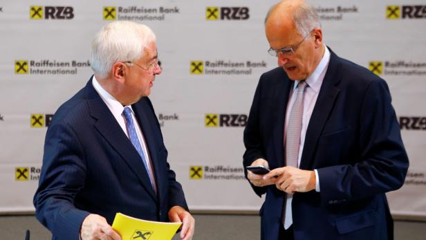 Zwei Männer in Anzügen unterhalten sich vor einem Hintergrund der Raiffeisen Bank International.