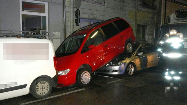 Ein roter Van steht auf einem silbernen Auto, während ein weißer Lieferwagen davor steht.