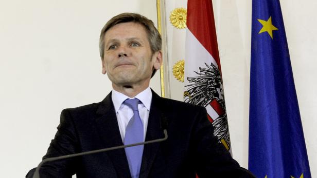 Ein Mann in Anzug steht vor der österreichischen und der EU-Flagge.